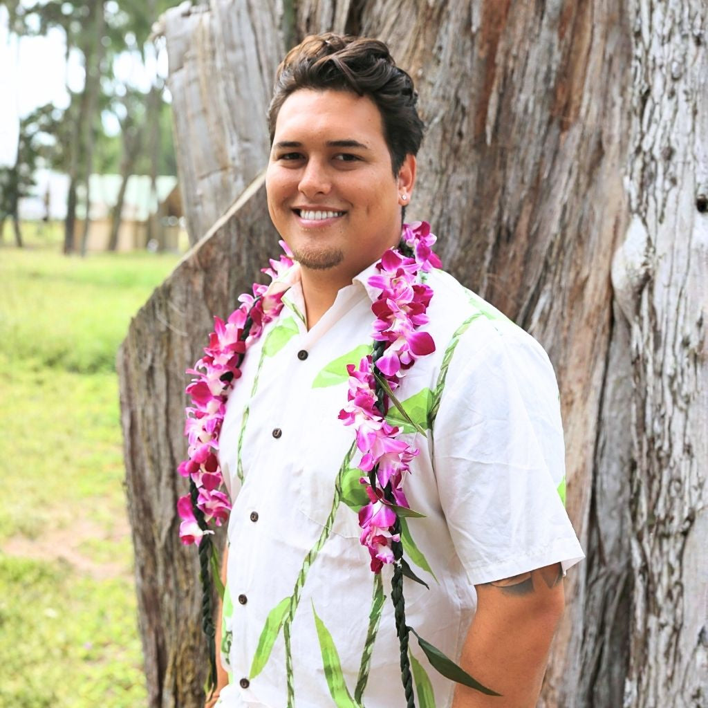 Man wearing a white shirt with ti leaf lei & purple orchid wrap.