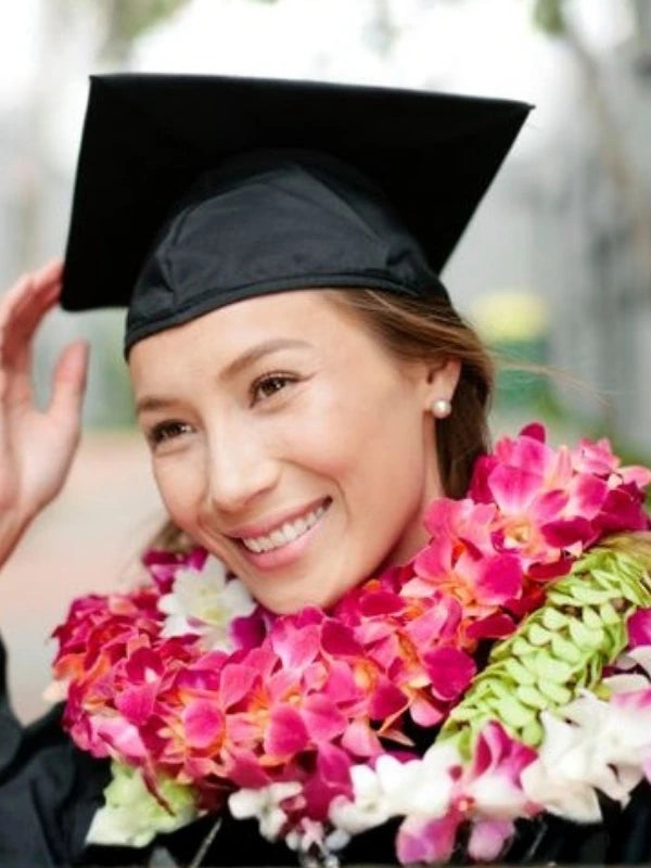 Graduate wearing a black cap and gown with colorful Hawaiian lei or lei necklaces for graduations