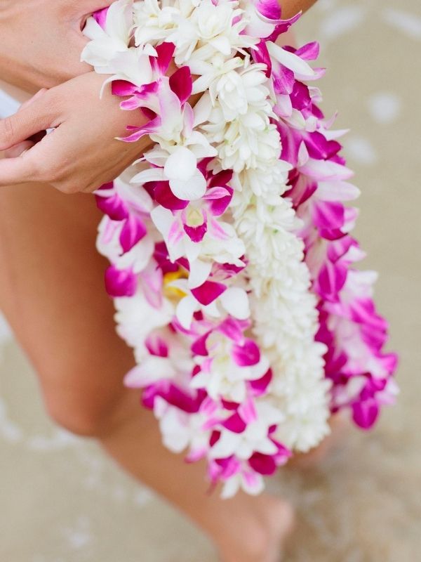 orchid lei and white flower lei held by a person on the beach background